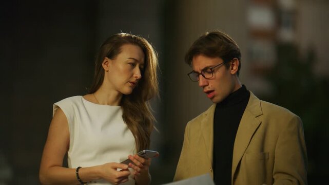 Business colleagues intently discuss a project, reviewing details on a smartphone. Their collaborative conversation unfolds in an urban outdoor environment.