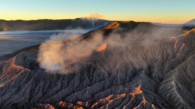 Dramatic sunrise bathes volcanic Bromo crater in warm gold. Steam rises from active vent, swirling gently