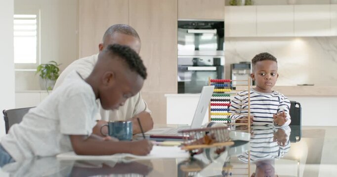 African American dad helping older son after starting homework at kitchen table with pencil abacus