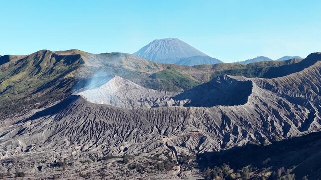 Steam rises from a volcanic Bromo Crater. Rugged terrain sprawls beneath a clear blue sky