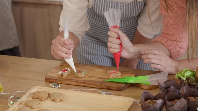 Gingerbread Cookie Decorating Close Up of Hands Piping Red and White Icing on Festive Biscuits During a Christmas Baking Activity in the Kitchen