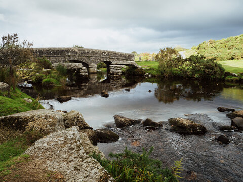 Old stone bridges on Dartmoor with river and rocks, and landscape beyond lit up warmly