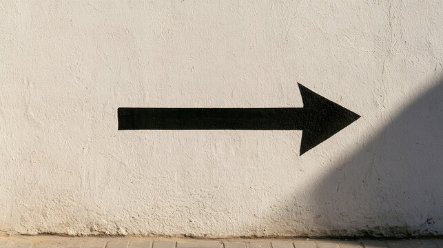 Black arrow painted on white textured wall pointing right directional sign symbol for business success navigation concept concept minimal modern clean graphic design sharp shadows sunlight exterior ur