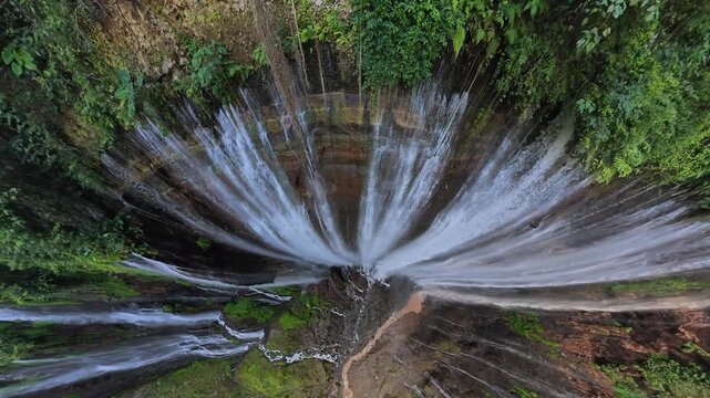 Fisheye aerial drone capture of Tumpak Sewu waterfall radial cascades and lush green cliff vegetation.