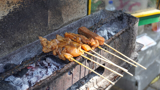 Traditional Indonesian satay kere skewered on bamboo sticks grilled over hot charcoal on street food vendor grill, authentic local culinary delicacy from Solo Central Java full of savory taste.