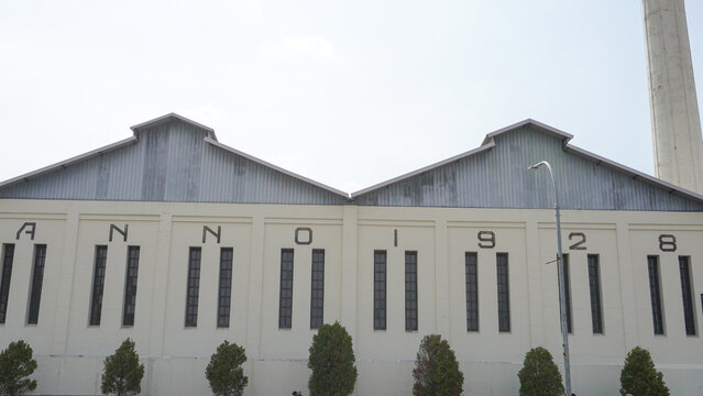 Exterior of historic De Tjolomadoe sugar factory with tall chimney stack, ANNO 1928 facade text, and Dutch colonial industrial architecture in Karanganyar, Solo, Central Java, Indonesia landmark.
