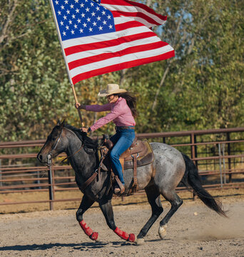 Cowgirl riding horse waving american flag in rodeo arena Southwest USA
