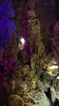 Vertical Video: Light shining through a distant cave opening, revealing a complex interior filled with jagged rock formations and towering ancient rock columns.