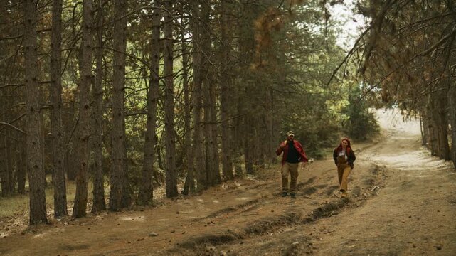 Couple hikes and talks along a forest trail with backpacks as their dog follows behind in slow motion.