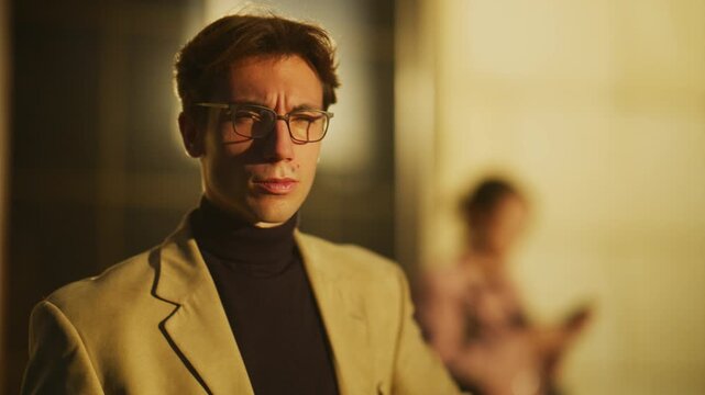 A stylish young man in glasses checks his watch and then engages in a focused phone conversation. He appears serious and professional while making a call on his smartphone.