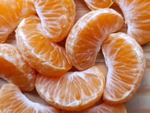 Close-up of fresh peeled mandarin orange segments on a wooden surface, showing juicy citrus flesh and delicate white pith. Healthy seasonal fruit associated with winter, Christmas and New Year holiday
