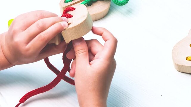 Close up of child hands threading lace through wooden toy Educational demonstrating fine motor skills development 4k resolution Hands eyes coordination Montessori sensorial activity Stacking Game