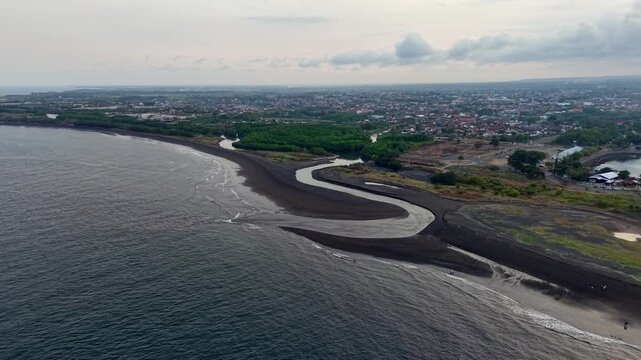 Aerial drone over Pantai Boom showing black sand curve, mangrove river, shoreline and distant city.