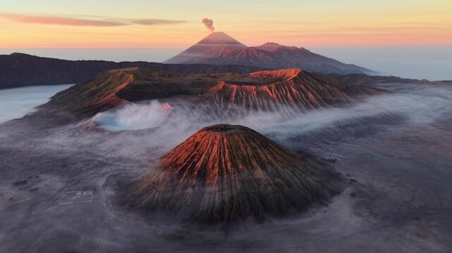 Misty peaks glow at dawn soft light. Steam rises from craters, swirling in cool air at Bromo