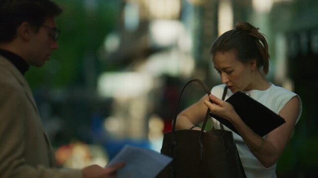 A focused businesswoman organizes her tablet and documents outdoors, preparing for an important task. She diligently arranges her work materials, reflecting professionalism and readiness.