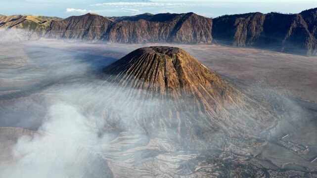 Volcanic Gunung Batok peak shrouded in misty clouds. Rugged terrain surrounds ancient, towering peak