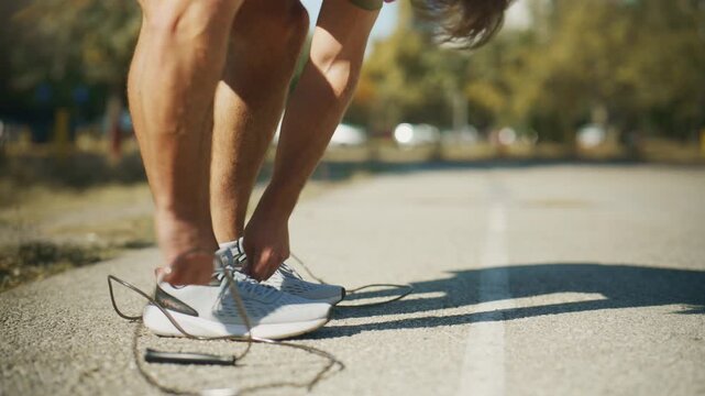 Man picks up a jump rope and bounces rhythmically on an outdoor track in slow motion during cardio training.