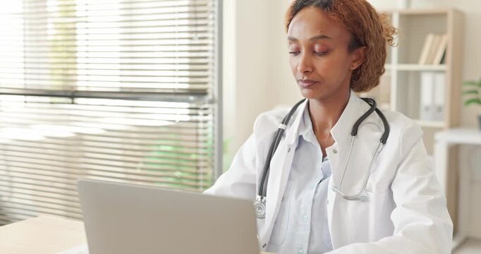 Female physician uses laptop for healthcare consultation. Stethoscope wearing doctor works at desk in clinic, reviewing medical records for patient support. Digital care support concept today.