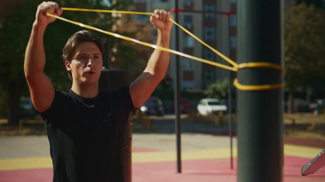 Man performs resistance band exercises at an outdoor gym, training shoulders and chest as the camera slowly zooms closer.