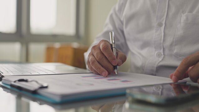 Businessman reviews financial charts, sales data report on desk in corporate office. Financial budget analysis, investment performance audit, commercial market research, strategic corporate planning.