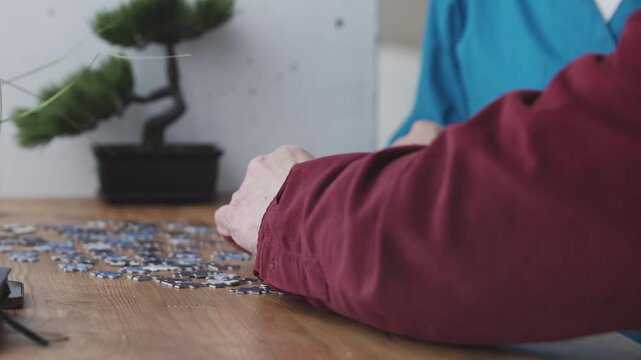 Female nurse keeps senior man company while connecting jigsaw puzzle pieces