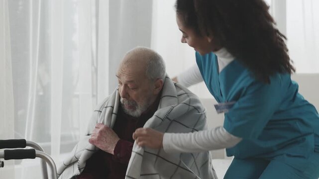 Caring young nurse brings blanket to elderly man, support and assistance