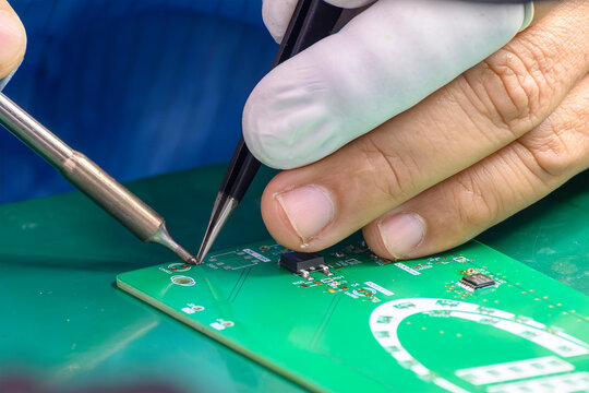 Close-up of a skilled operator wearing rubber finger cots soldering an electronic PCB board