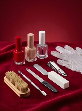 Manicure set and nail polish bottles arranged on red velvet fabric floor