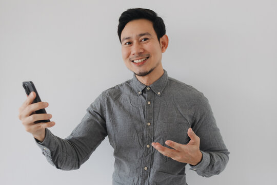Confident Asian man smiles, holding a smartphone and gesturing to present information.