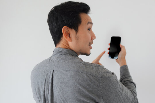 Engaged Asian man in grey shirt points at smartphone, showing content.