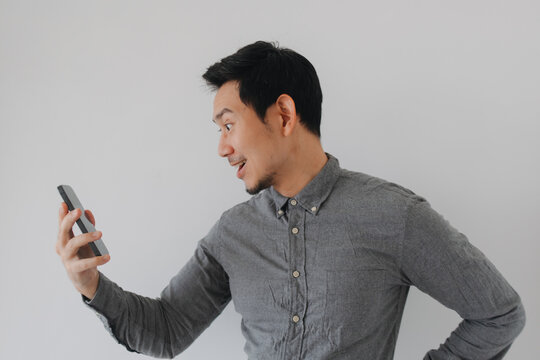 Excited young Asian man looking at his smartphone with a surprised and happy expression.