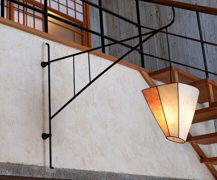 A decorative hanging lantern is illuminated on a textured wall near a staircase.