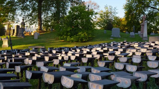 Repeating light fixtures form a grid across cemetery grass. Black housings and pale circular lenses fill the foreground with headstones and trees behind.