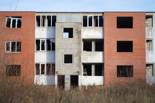 Unfinished multistory brick and concrete building with empty window openings. Abandoned construction site. Urban decay and building neglect. Architecture, redevelopment and housing concept.
