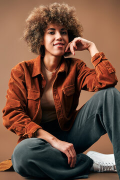 Stylish woman in rust corduroy jacket sitting on floor.