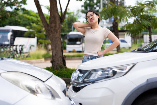A woman holds her neck beside two white cars parked close together outdoors, illustrating possible car accident discomfort, vehicle safety concerns, and auto insurance claim documentation.