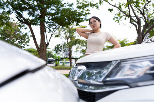 A young woman touches the back of her neck between two white cars in a leafy outdoor setting, illustrating discomfort and commercial themes of road safety, auto insurance, and vehicle incidents.