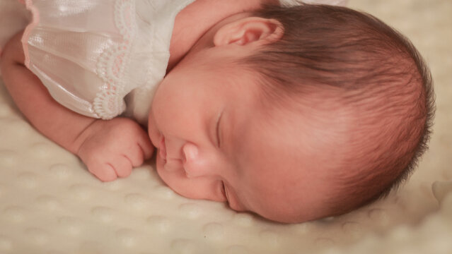 Close up newborn baby, infant, sleeping peacefully on a soft white blanket, quiet moment of rest, comfort, and early infant development.