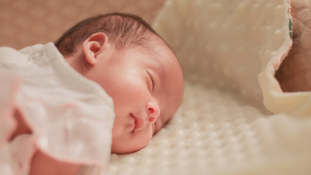 Close up newborn baby, infant, sleeping peacefully on a soft white blanket, quiet moment of rest, comfort, and early infant development.