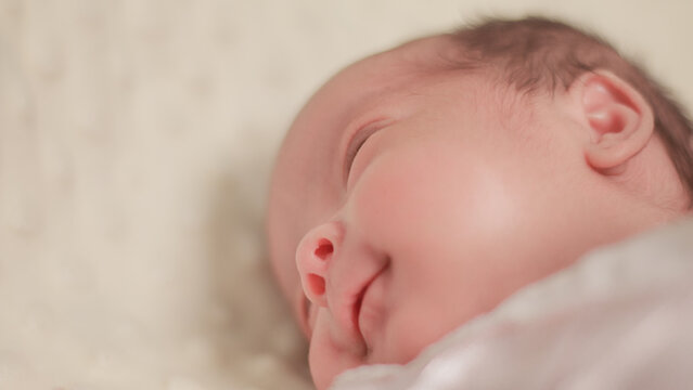 Close up newborn baby, infant, sleeping peacefully on a soft white blanket, quiet moment of rest, comfort, and early infant development.