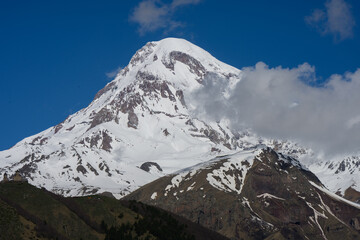Majestic snow peak of Mount Kazbek with Gergeti Trinity Church on hill, Georgia. Famous ancient landmark, orthodox stone temple in Caucasus mountains. Caucasian tourism theme © GRON777