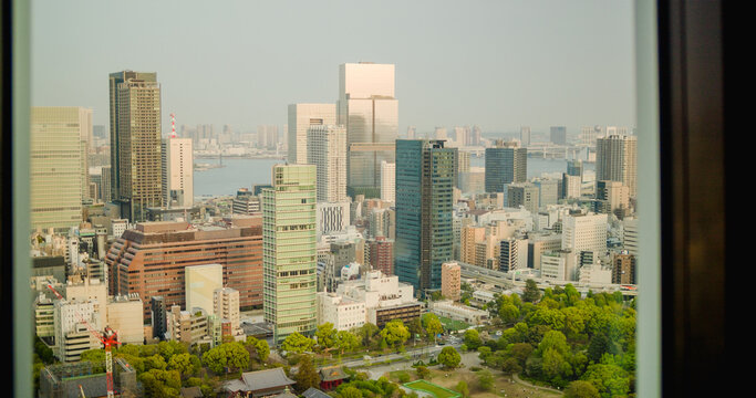 Tokyo, Japan - 19 April 2025: View of the dense urban skyline of Tokyo featuring modern skyscrapers, glass office buildings, and lush green park areas under a clear sky.