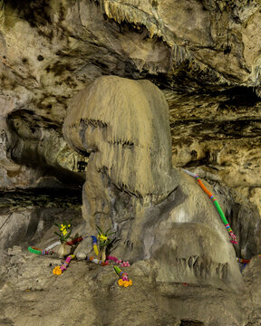 Sacred stalagmite rock formation adorned with colorful fabrics and floral offerings in Tham Krasae cave