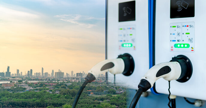 Electric vehicle charging station overlooking a modern city at sunset, clean energy infrastructure supporting sustainable urban transportation, lower carbon emissions and greener mobility.