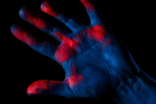 Blue human hand covered with red fingerprints on a black background, concept of influence and propaganda