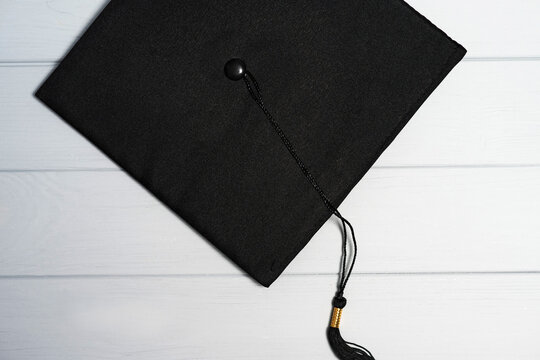 Black mortarboard with hanging tassel lying on gray white wooden boards, graduation day flat lay