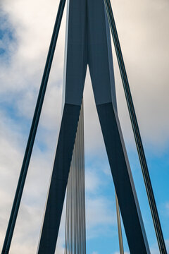Rotterdam, Zuid-Holland, Netherlands - 25 February 2023: View of the structural pylon and steel cables of the Erasmusbrug bridge against a cloudy blue sky.