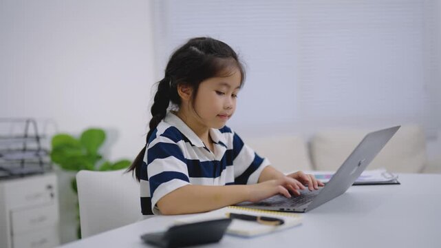 Young girl using calculator and laptop for homework or study in bright modern home environment