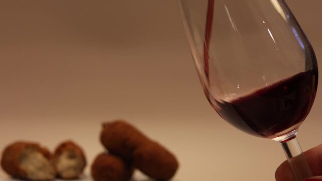 Red wine pouring into a crystal glass next to freshly fried croquettes on a table