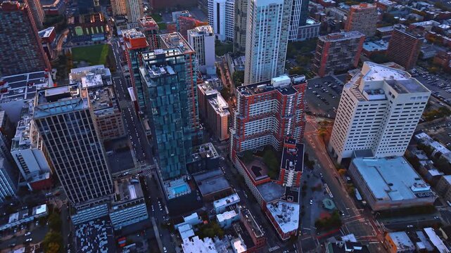 Glass apartment towers stand among downtown Jersey City buildings. A blue pool sits between blocks below the steep view with rooftop equipment and intersecting roads nearby.